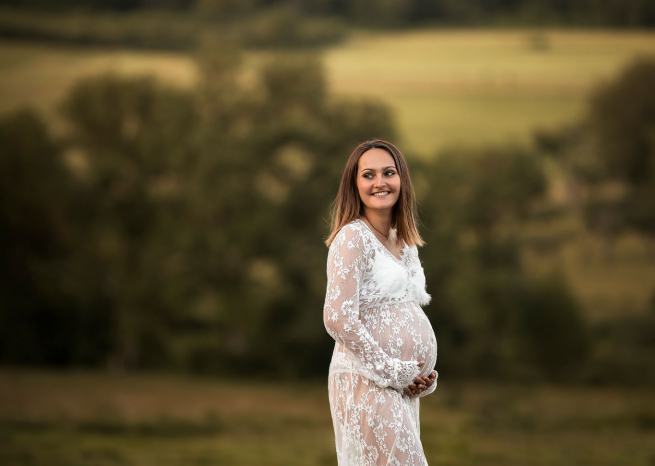 Shooting photo maternité à Bouxurulles : femme enceinte en robe de dentelle blanche posant dans un champ au coucher du soleil.