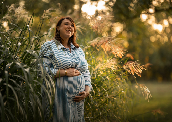 Femme enceinte posant dans une robe rayée au milieu d'un paysage naturel sauvage lors d'une séance photo à Nancy.