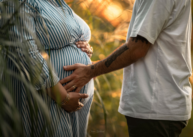 Gros plan artistique des mains des futurs parents sur le ventre de la maman, robe rayée et tatouage visible