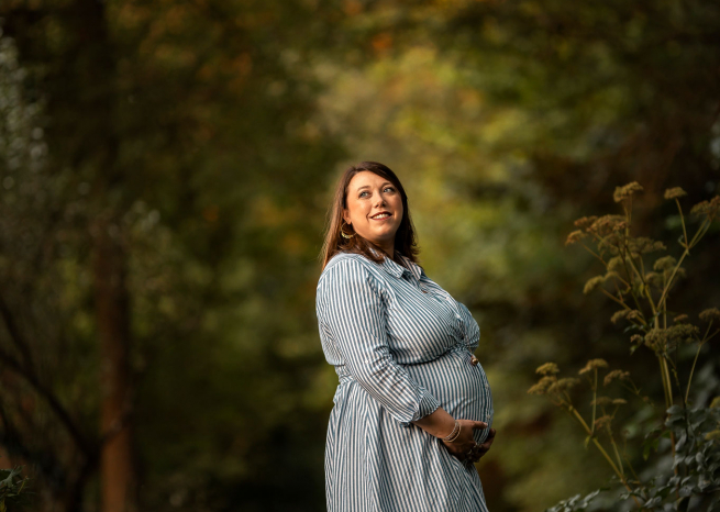Portrait d'une femme enceinte souriante lors d'une séance photo de grossesse en extérieur près de Nancy, lumière dorée de fin de journée.