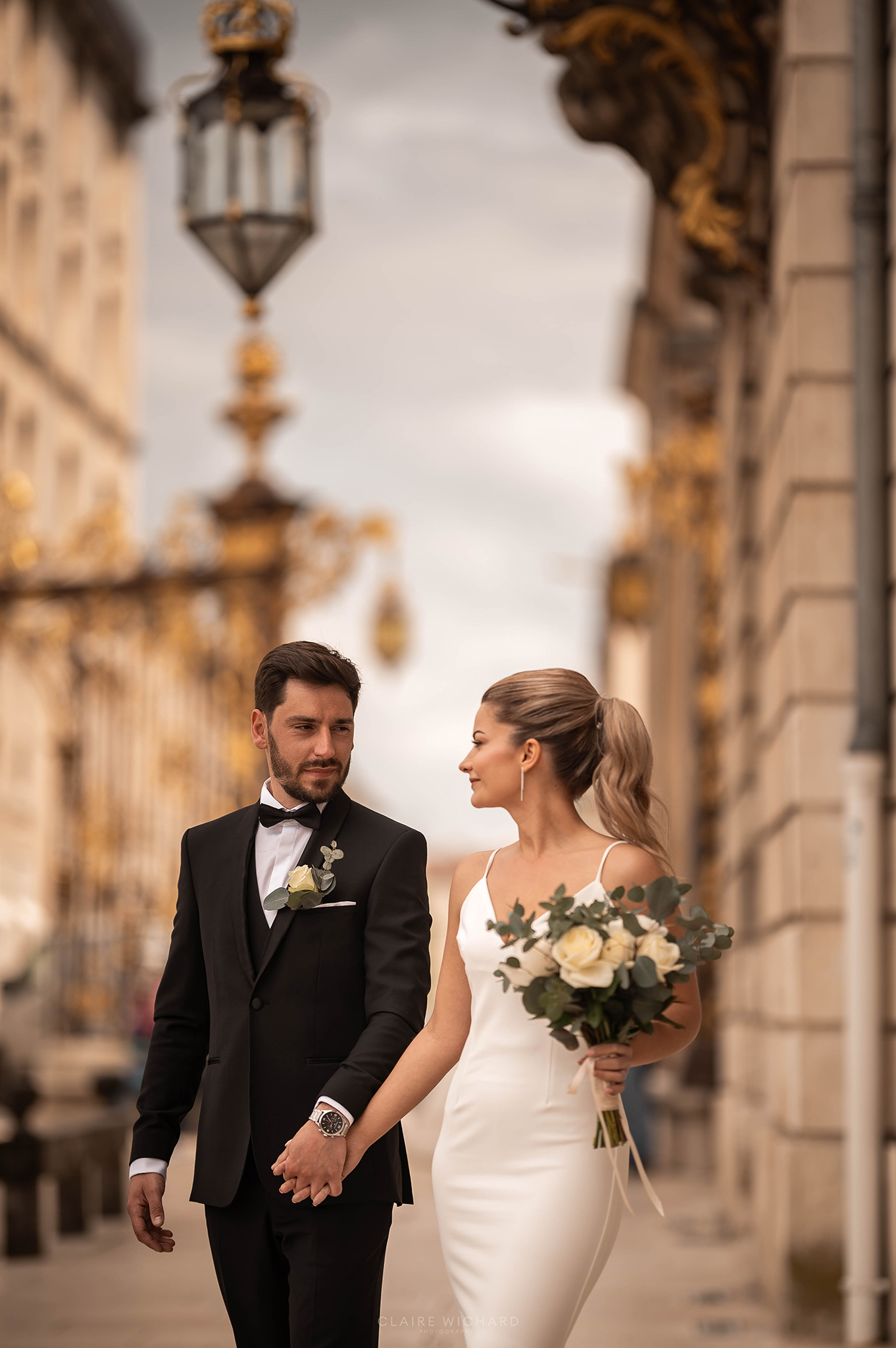 Couple de mariés élégant marchant main dans la main devant les grilles monumentales de la Place Stanislas à Nancy