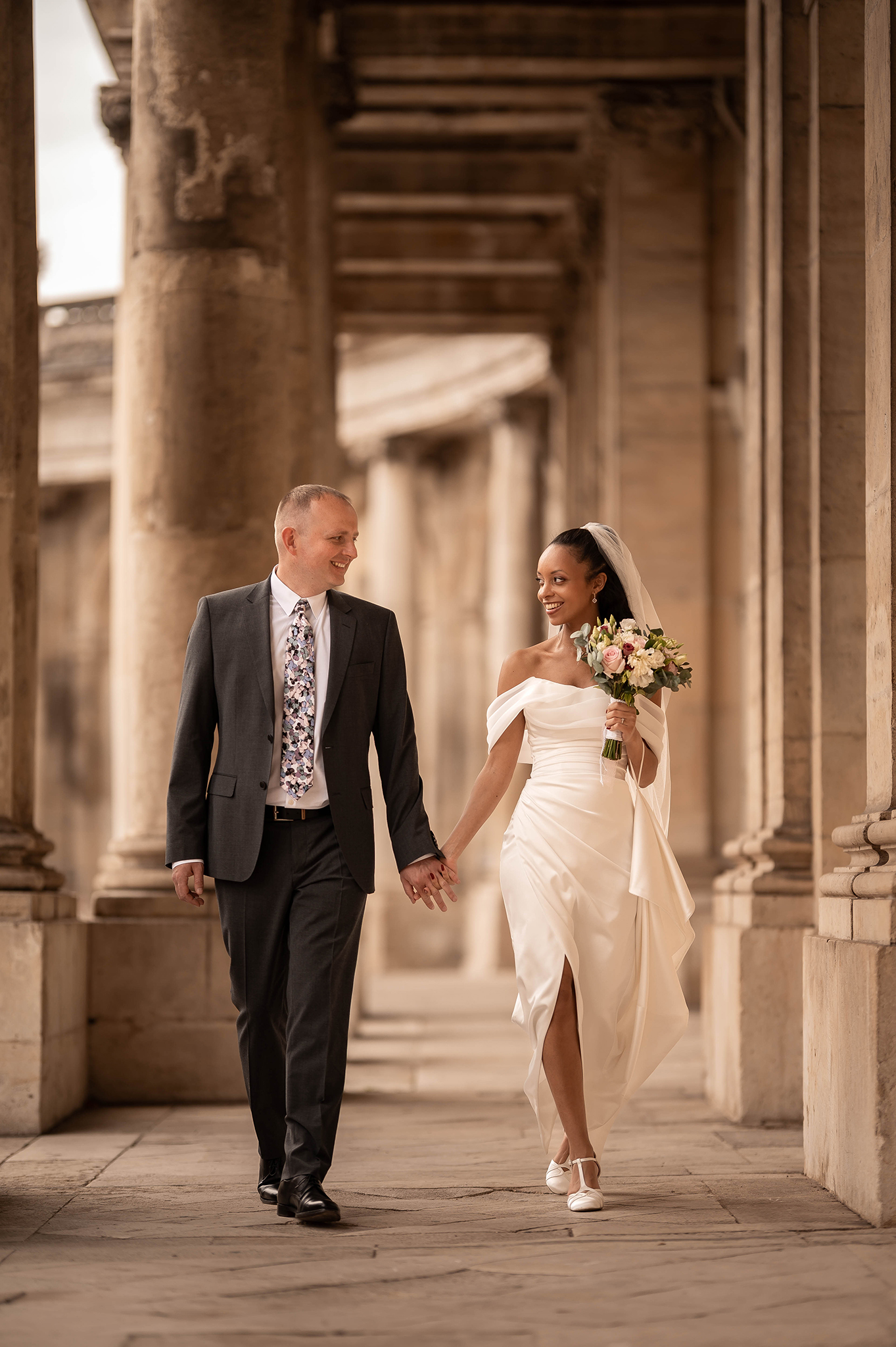 Couple de mariés marchant main dans la main sous les colonnades du Palais du Gouvernement à Nancy, style lifestyle