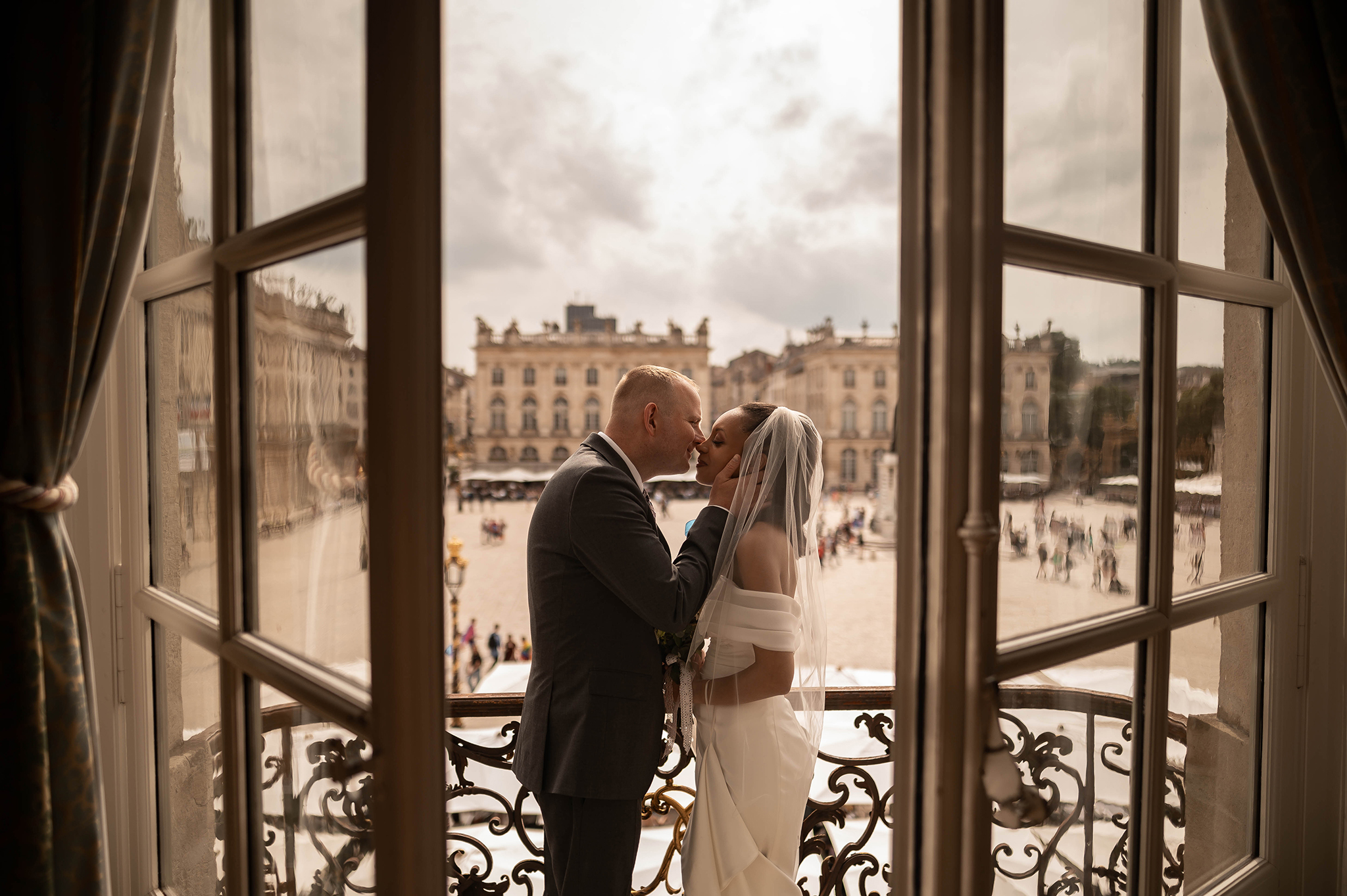 Moment romantique des mariés sur le balcon de l'Hôtel de la Reine avec vue sur les bâtiments historiques de la Place Stanislas à Nancy