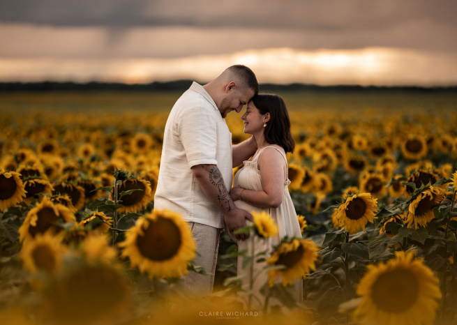 Couple de futurs parents s'enlaçant dans un champ de tournesols au coucher du soleil, séance photo grossesse à Nancy.