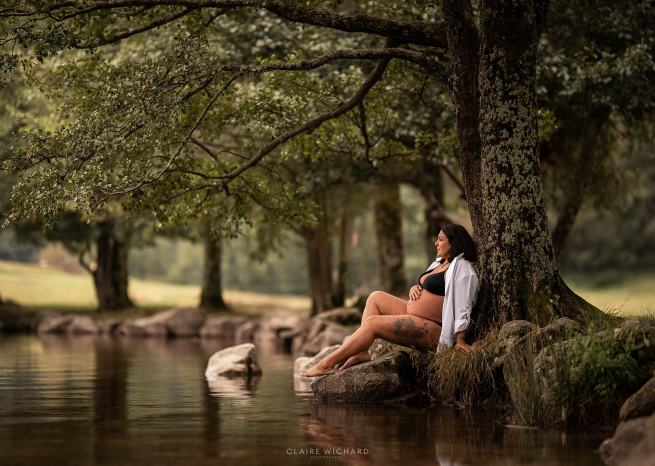 Future maman assise sur un rocher au bord de l'eau, séance photo maternité dans les Vosges