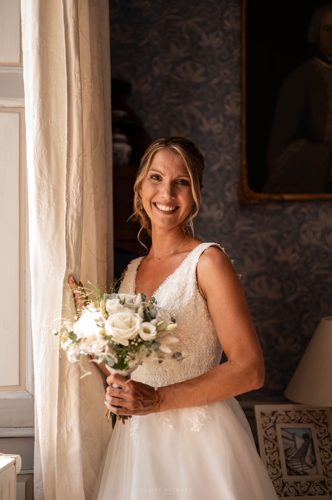 Portrait souriant de la mariée avec son bouquet dans les salons historiques du Château d'Autigny-la-Tour.