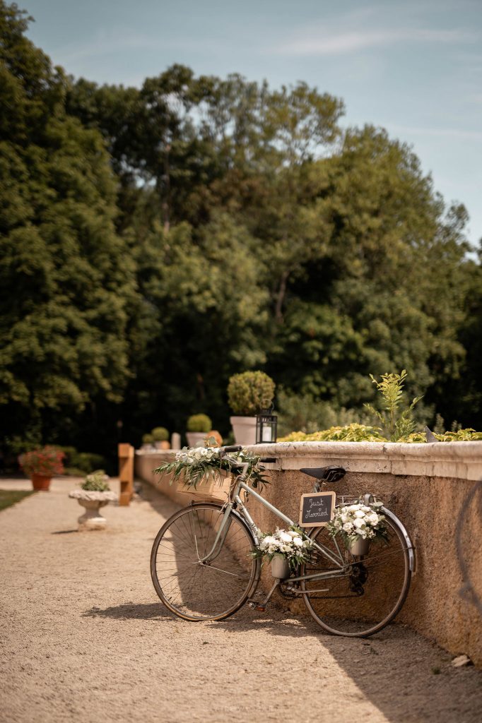 Décoration de mariage champêtre avec un vélo vintage fleuri et panneau Just Married devant un mur en pierre, au château d'Autigny-la-tour