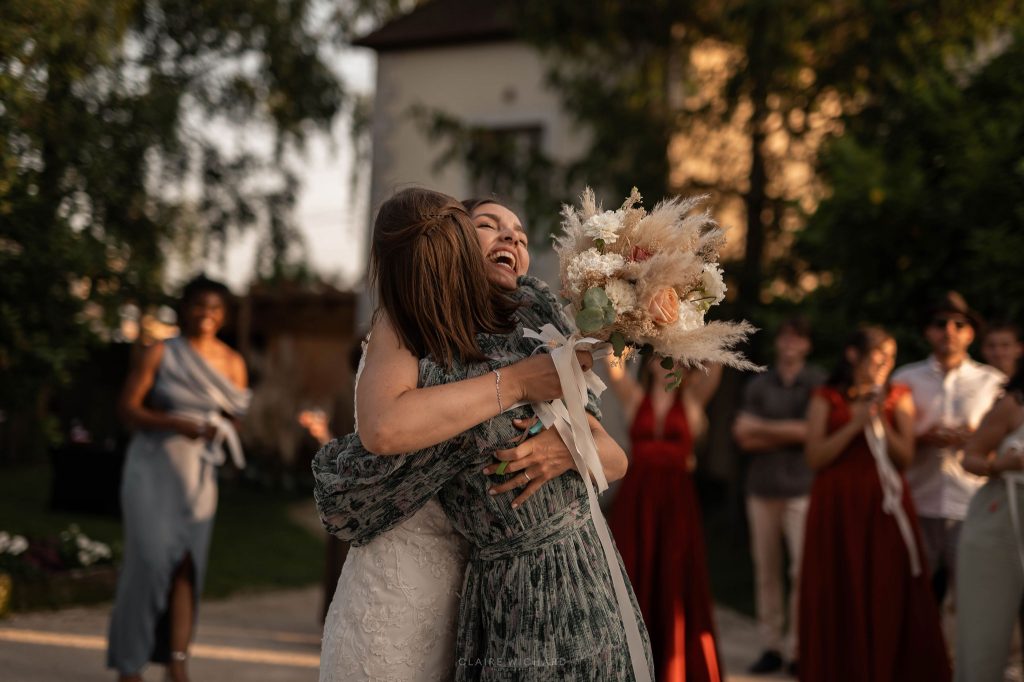 Mariée serrant chaleureusement dans ses bras l'invitée ayant attrapé le bouquet lors du vin d'honneur au Château d'Aboncourt, photographe mariage Nancy.