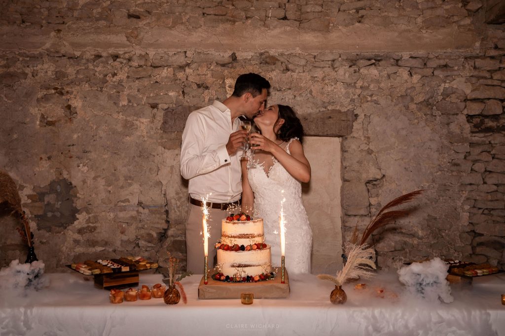Photographie artistique de mariage : mariés s'embrassant devant leur wedding cake au chateau ferme d'aboncourt en meurthe et moselle