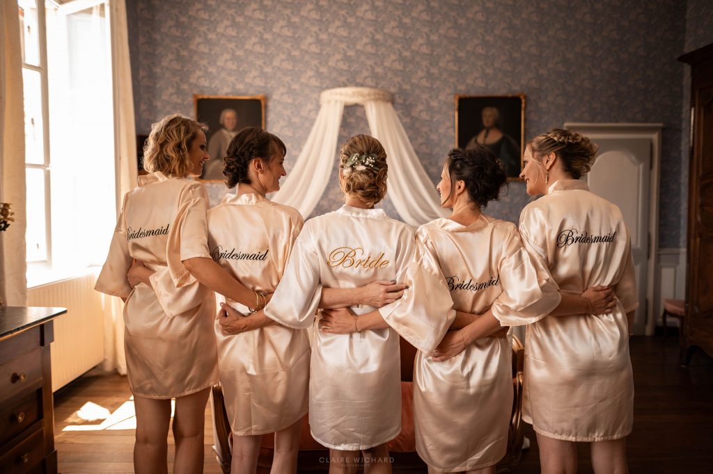 La mariée et ses demoiselles d'honneur de dos portant des peignoirs en satin personnalisés lors des préparatifs de mariage au château d'autigny-la-tour