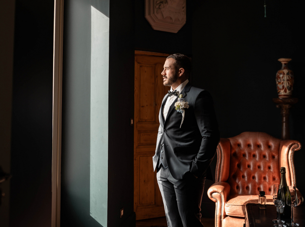 Photographe mariage Nancy : portrait élégant d'un homme en costume se tenant de côté près d'une fenêtre.
