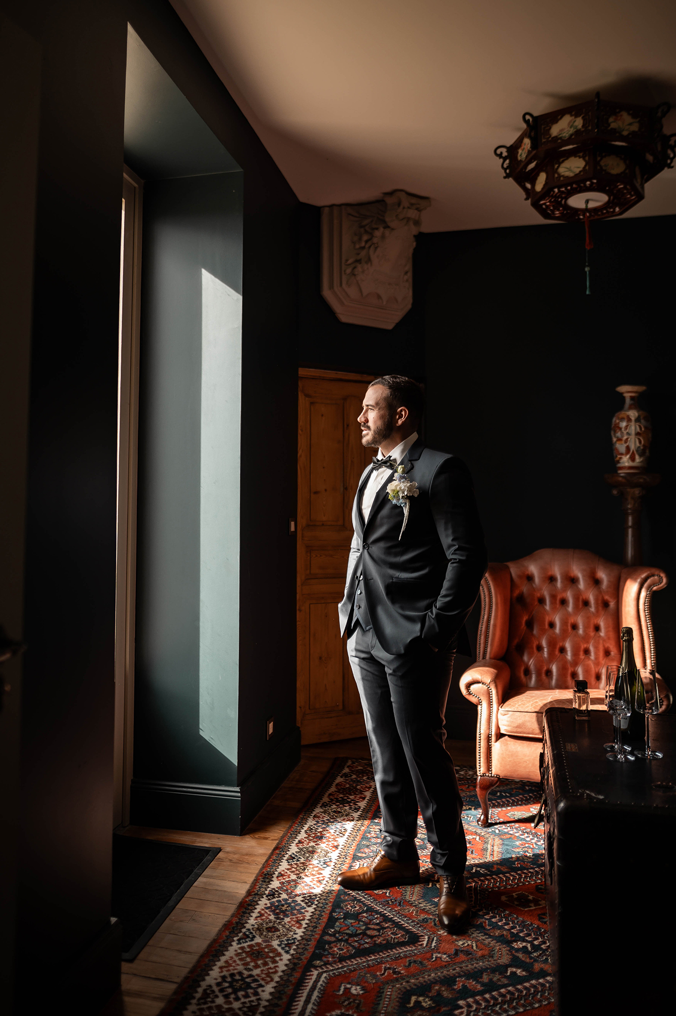 Photographe mariage Nancy : portrait élégant d'un homme en costume se tenant de côté près d'une fenêtre.