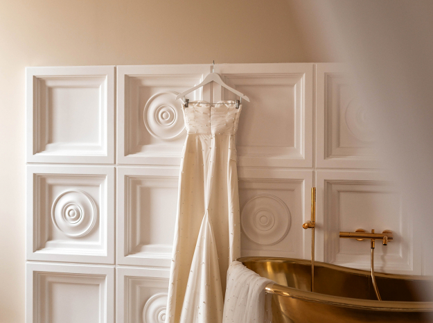 Photographie de détails de mariage : robe de mariée suspendue à côté d'une baignoire dorée dans un intérieur élégant à Nancy.