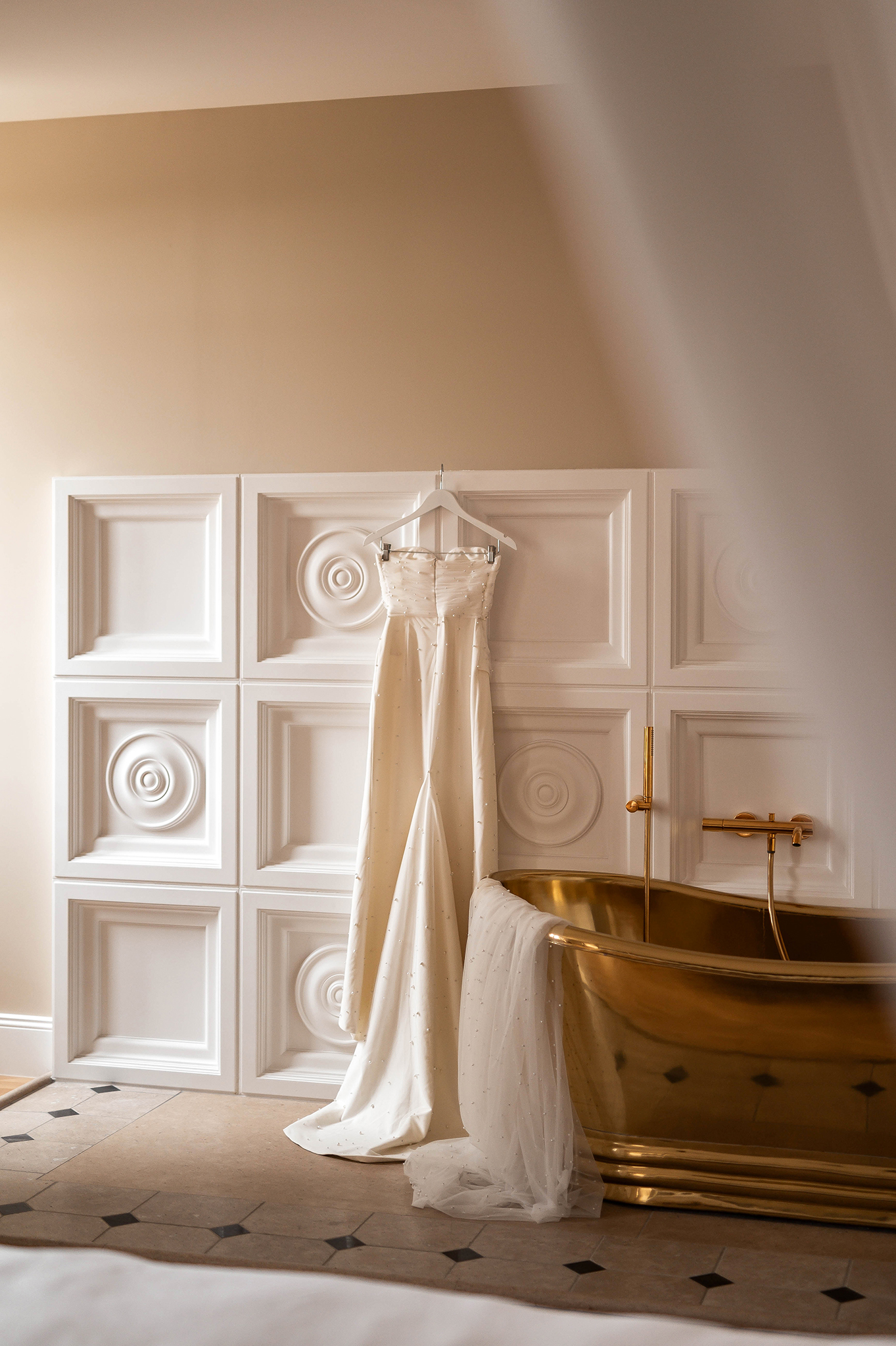 Photographie de détails de mariage : robe de mariée suspendue à côté d'une baignoire dorée dans un intérieur élégant à Nancy.
