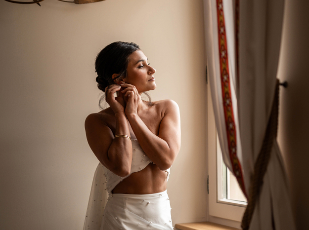 Mariée élégante mettant ses boucles d'oreilles devant une fenêtres en lorraine