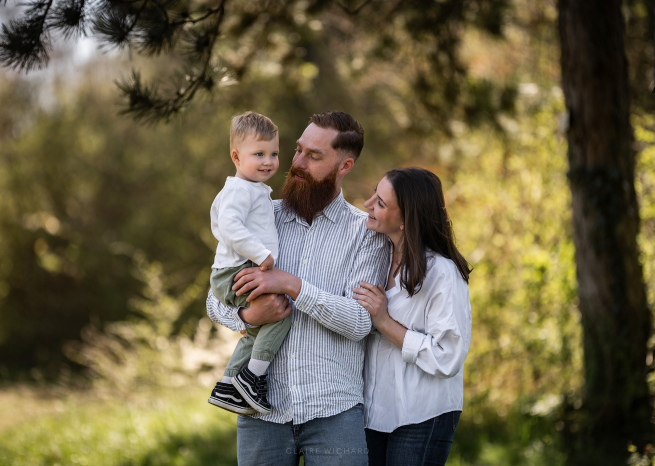 Photographe lifestyle à Nancy : parents portant leur enfant dans les bras dans une foret de la colline de sion