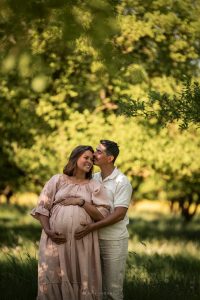 Séance photo de couple enceinte dans les vergers de Meurthe-et-Moselle, futur papa embrassant la maman sous une lumière dorée près de Nancy.