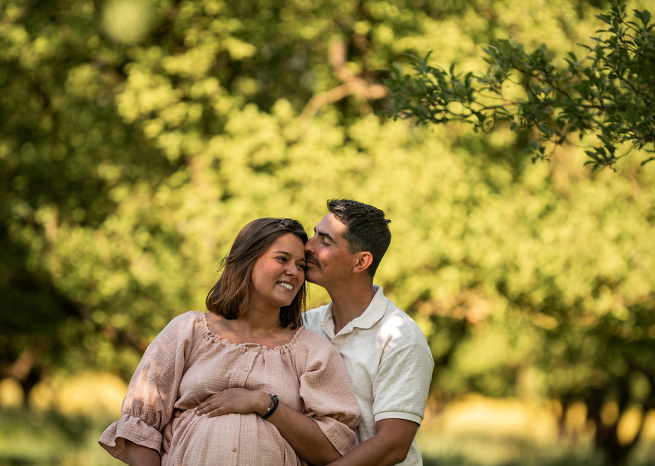 Séance photo de couple enceinte dans les vergers de Meurthe-et-Moselle, futur papa embrassant la maman sous une lumière dorée près de Nancy.