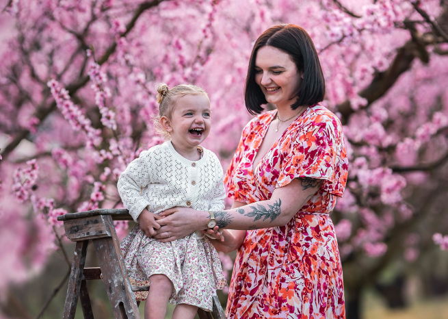 femme et sa petite fille rigolant sur un escabeau devant des mirabelliers roses en fleurs, en meurthe-et-moselle