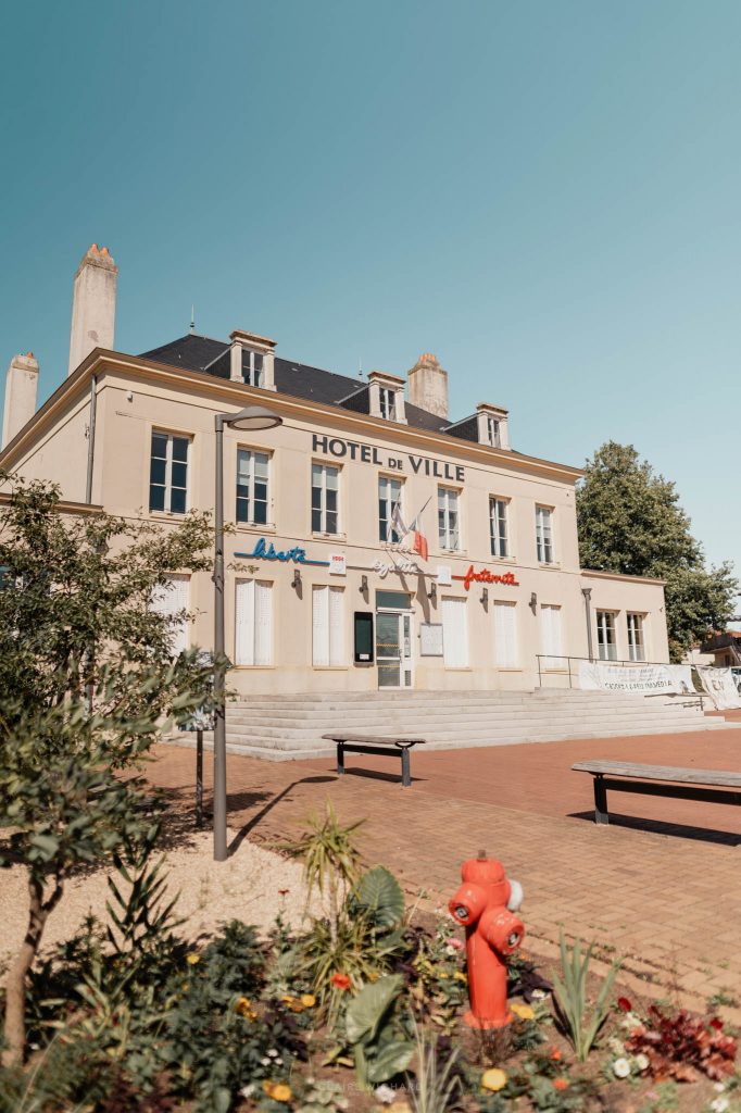 Façade extérieure ensoleillée de l'Hôtel de Ville de Jarny avec ses parterres de fleurs au premier plan.
