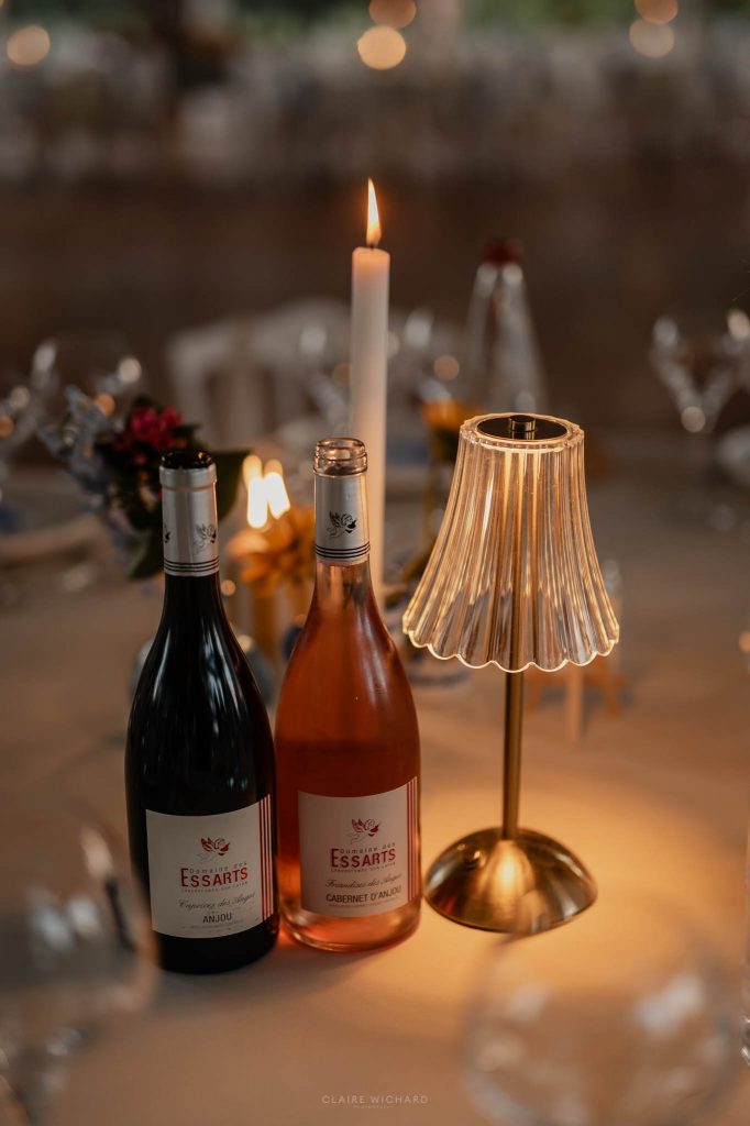 Bouteilles de vin d'Anjou et lampe de table sans fil plissée éclairant chaleureusement une table de réception en soirée