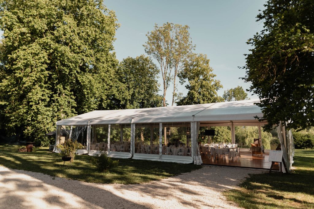 Grand chapiteau de mariage transparent installé sur une pelouse verdoyante à l'orée d'un parc arboré