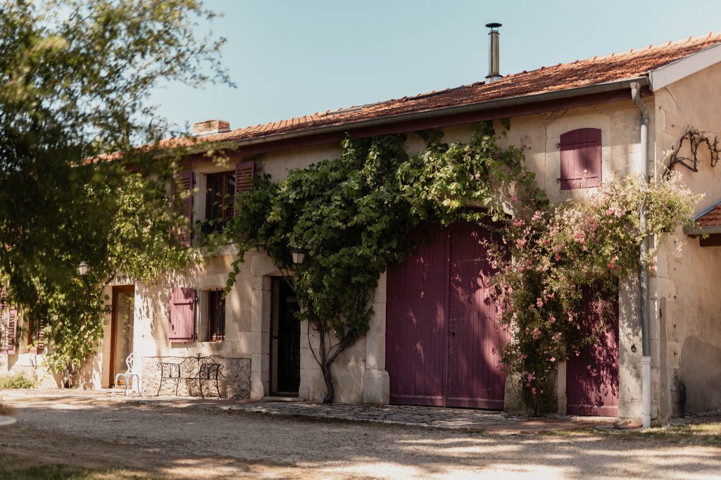 Bâtisse ancienne en pierre avec volets bordeaux et végétation grimpante au domaine du Château des Aulnes
