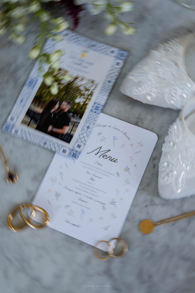 Détails de mariage sur table en marbre avec le menu, les alliances en or, les bijoux et les chaussures de la mariée au chateau des aulnes