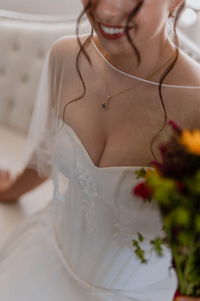 Gros plan sur le bustier et le voile en tulle brodé d'une mariée à Nancy portant un collier en or et tenant son bouquet