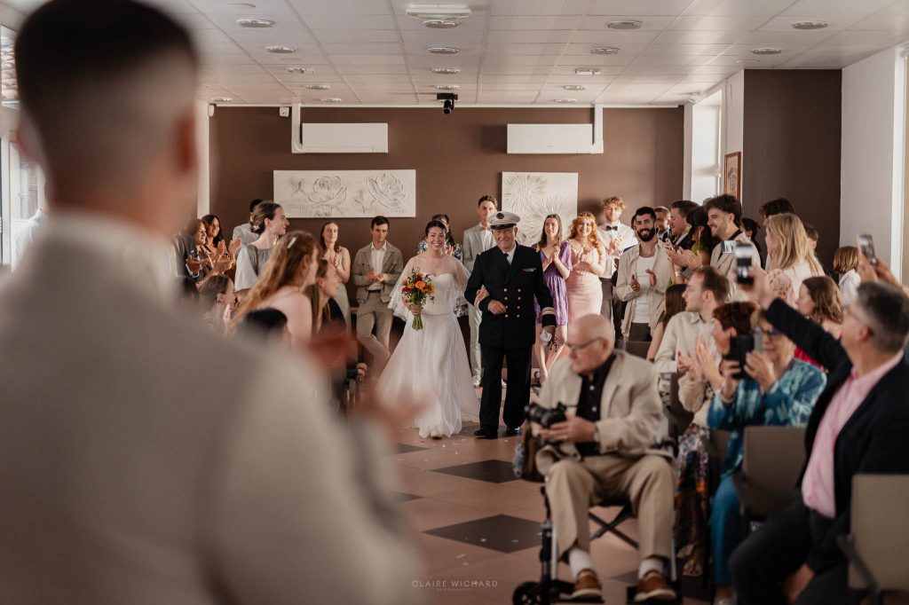 Entrée de la mariée au bras de son père en costume de marin sous les applaudissements des invités à la mairie de Jarny