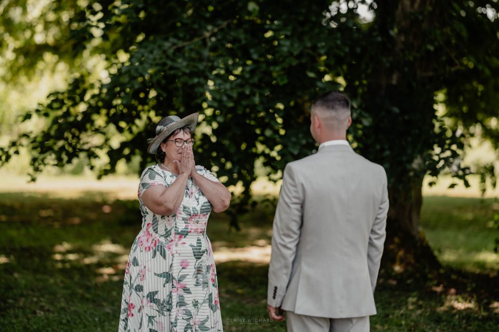 Émotion d'une mère découvrant son fils en costume de marié lors du first look dans le parc arboré du chateau des aulnes en Lorraine