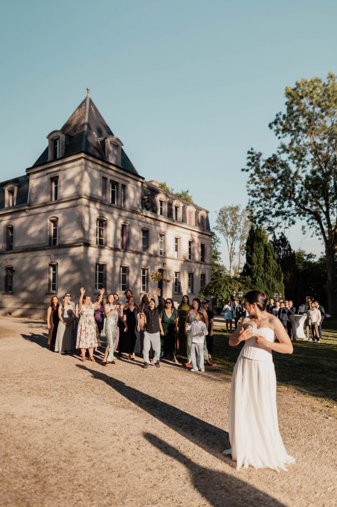 La mariée de dos s'apprête à lancer son bouquet à ses invitées réunies devant la façade d'un château en Lorraine.