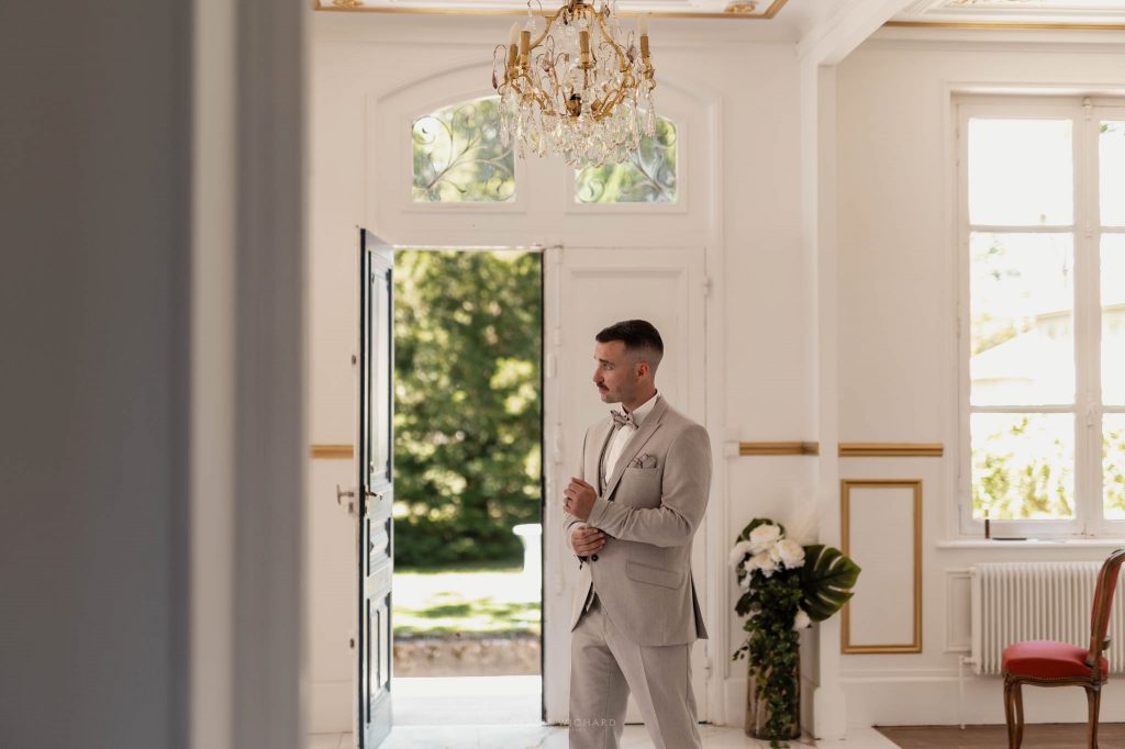 Le marié debout dans le hall d'entrée lumineux du Château des Aulnes, prêt pour sa journée de mariage