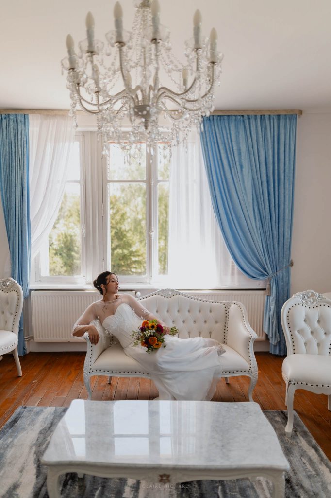 La mariée allongée sur une méridienne blanche, tenant son bouquet de fleurs colorées au Château des Aulnes