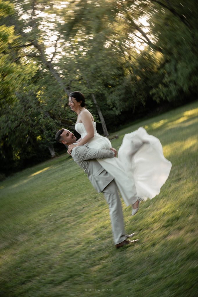 Photo artistique avec effet créatif de mouvement où le marié fait tourner sa femme dans ses bras au milieu du parc du chateau des aulnes