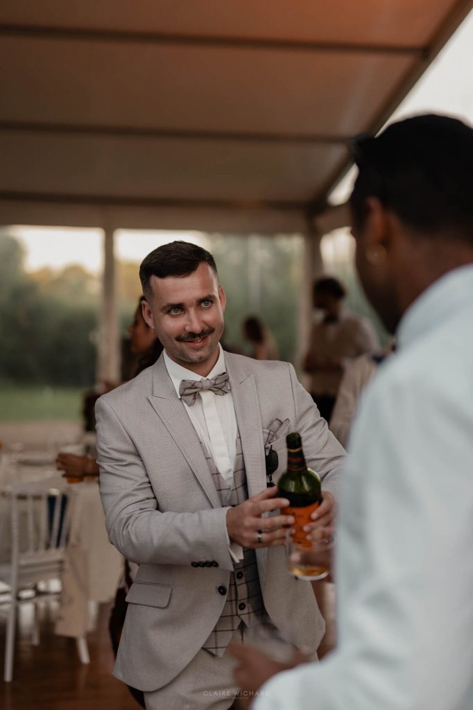 Le marié en costume beige discute un verre à la main avec ses invités lors d'un mariage à Nancy en Lorraine.