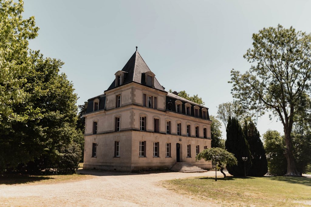 Vue d'ensemble du Château des Aulnes dans son parc arboré sous un ciel bleu pour un mariage en Lorraine
