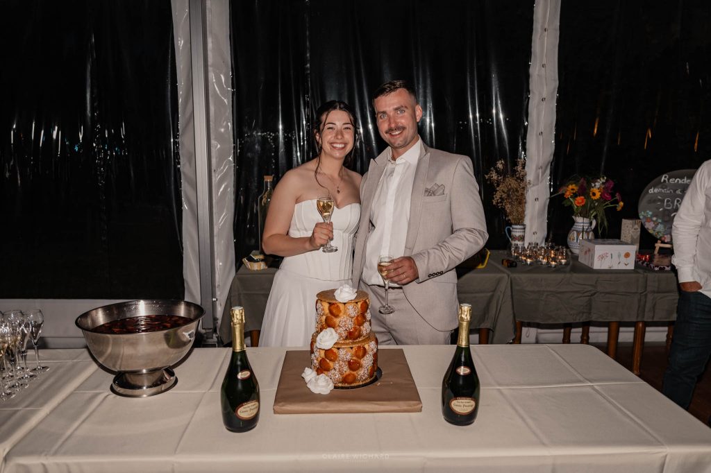 Les mariés posent tout sourire avec leurs flûtes de champagne devant leur pièce montée en choux traditionnelle à nancy