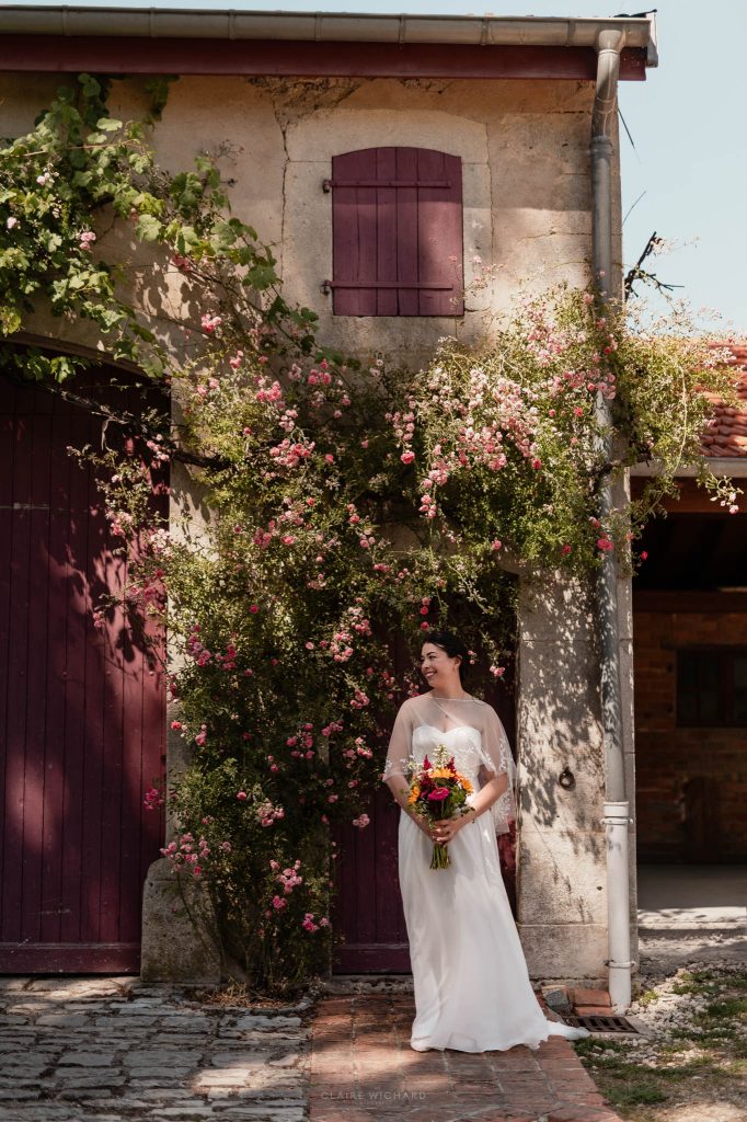 La mariée pose avec son bouquet devant un grand rosier en fleurs et les murs en pierre du domaine en Lorraine