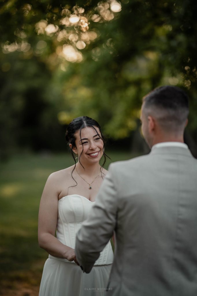 Portrait de la mariée aux cheveux bruns relevés, souriant avec douceur à son mari pendant leur séance photo.
