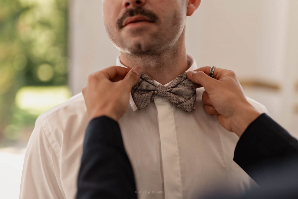 Gros plan sur les mains ajustant le nœud papillon à motifs d'un marié pendant ses préparatifs de mariage en Lorraine