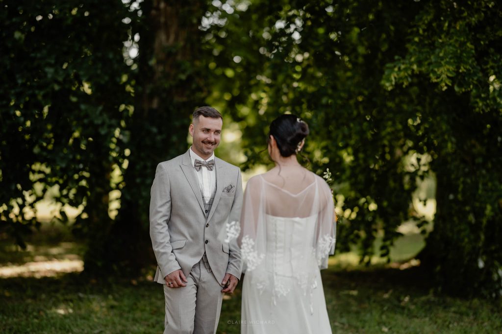 Le marié ému avec un grand sourire regarde sa future femme en robe blanche pendant la découverte de mariage