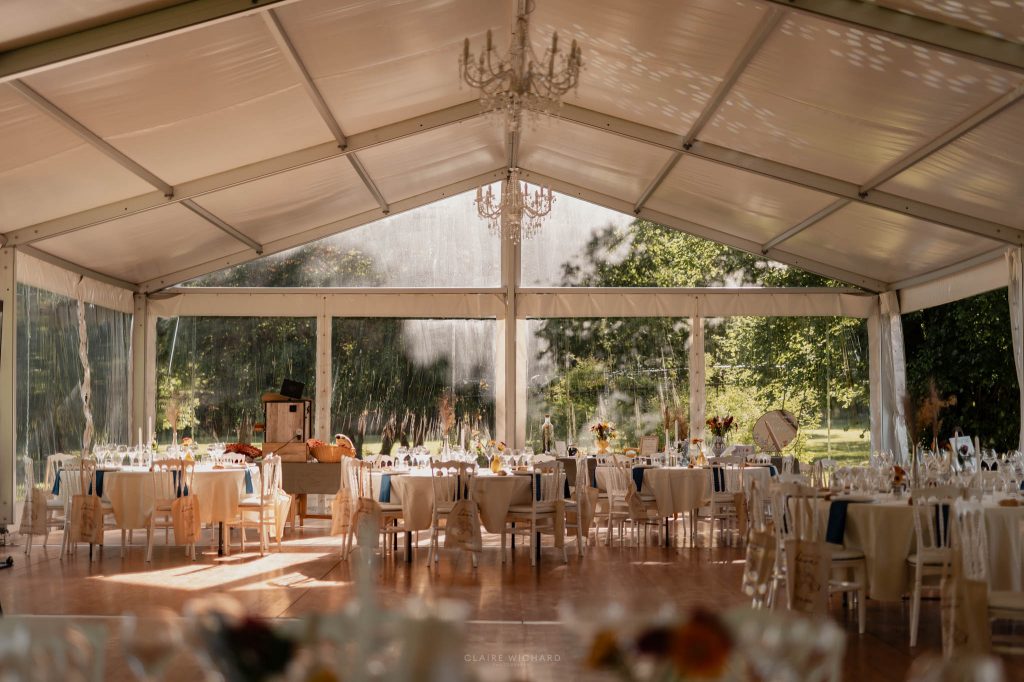 Vue d'ensemble des tables rondes dressées sous un chapiteau de mariage avec des lustres en cristal élégants dans le grand est