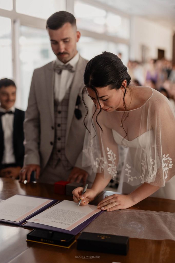 Gros plan sur la mariée signant les documents officiels du registre de mariage à la mairie de Jarny sous les yeux du marié.