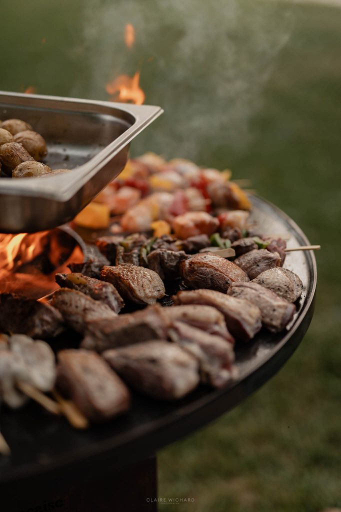 Gros plan sur les viandes et brochettes en train de griller sur un brasero extérieur lors d'une réception de mariage par le traiteur l'envol des sens