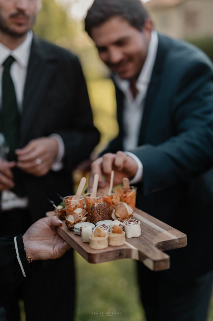 Un invité se sert sur un plateau en bois de pièces de cocktail salées présentées par le traiteur l'envol des sens lors du vin d'honneur
