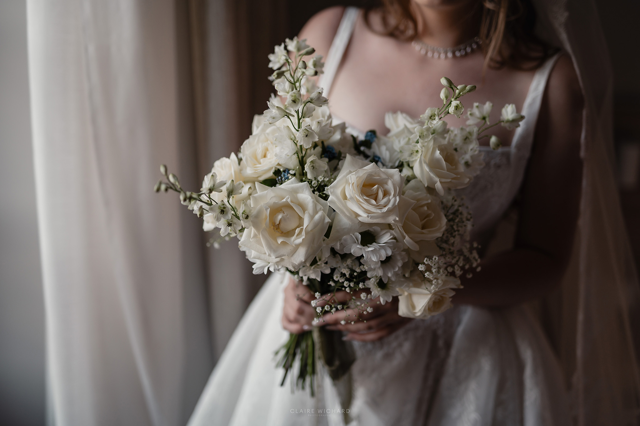 Portrait de la mariée tenant son bouquet de fleurs blanches devant les grandes fenêtres de l'Abbaye des Prémontrés, photo Claire Wichard photographe mariage Lorraine