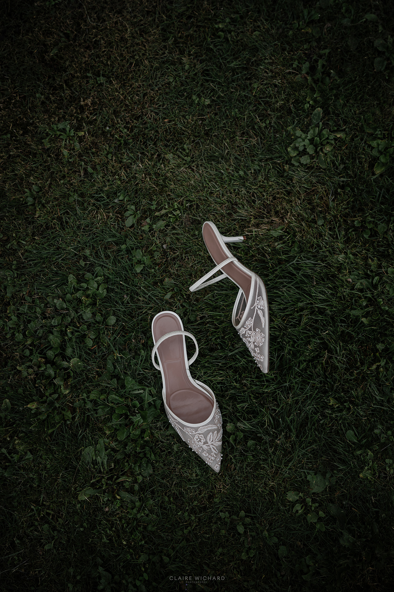 Paire d'escarpins de mariée élégants ornés de broderies florales posés sur la pelouse des jardins de l'Abbaye des Prémontrés, par Claire Wichard photographe de mariage en Lorraine