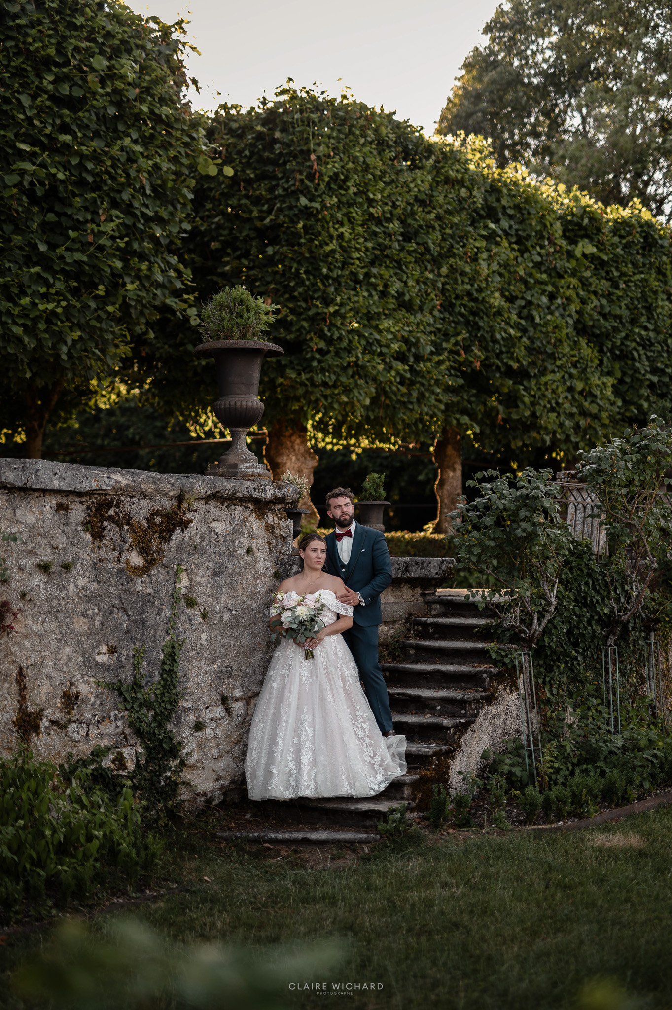 Photographie du couple de mariés posant sur l'escalier en pierre donnant sur le parc boisé du Château de Boucq en Lorraine