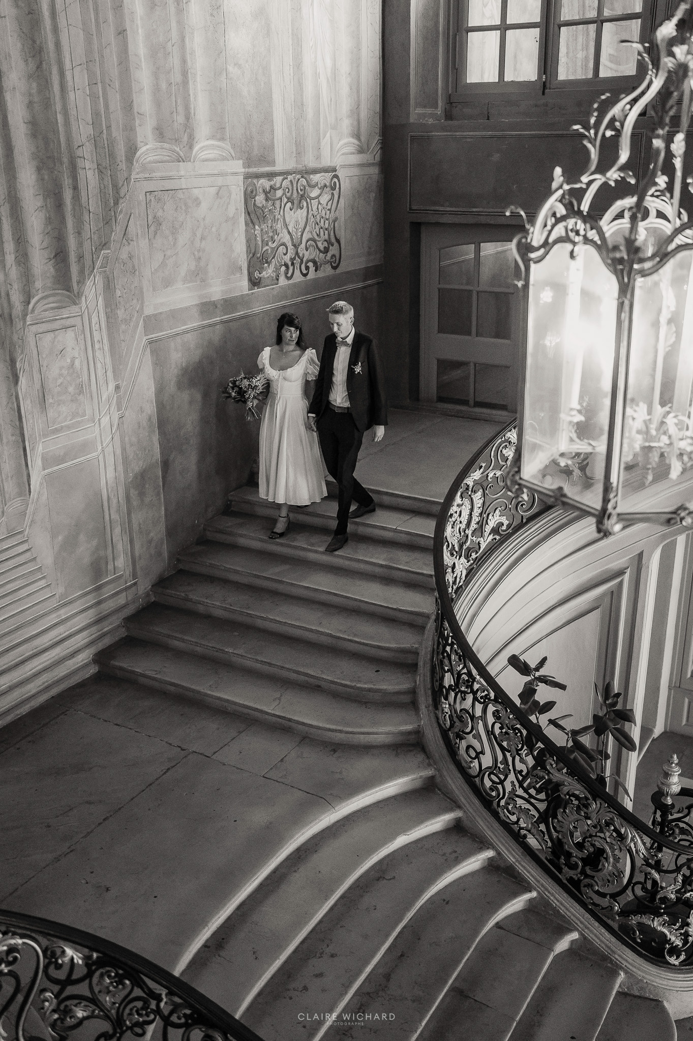 Photo en noir et blanc d'un couple de mariés descendant le grand escalier monumental de la mairie de Nancy après leur mariage civil.